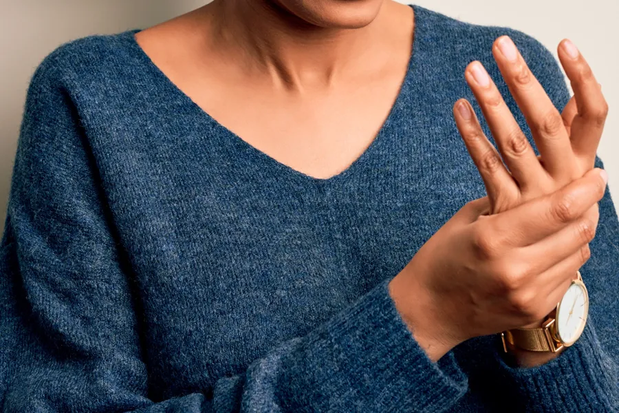 Arthritis-Doctor Close up of a woman in a blue sweater massaging one aching hand with the other. Get help for arthritis from Vitality Medical in Seattle.