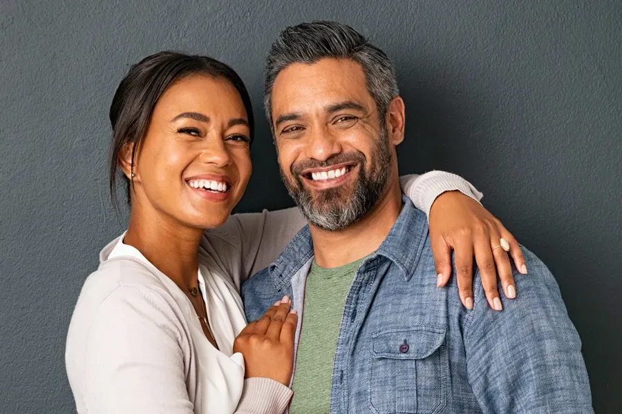 Bioidentical-Hormone-Therapy-Doctor A middle-aged couple with their arms around each other standing against a gray background and smiling, happy with the bioidentical hormone therapy they received from Vitality Medical in Seattle.