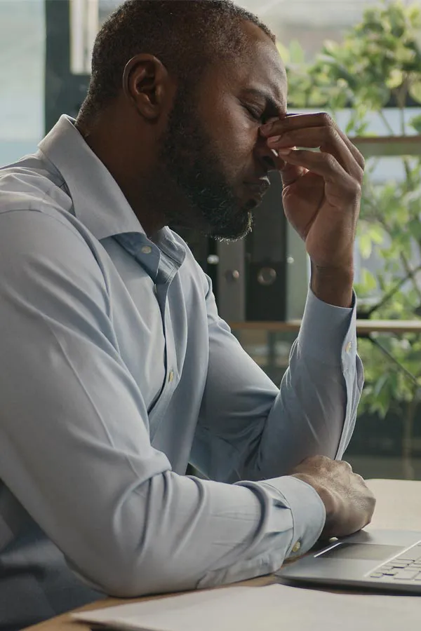 Chronic-Disease-Treatment A middle-aged black man sits at his desk holding his forehead in exhaustion. Get treatment for chronic disease from Vitality Medical in Seattle.