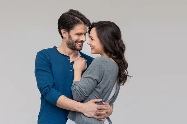 Erectile-Dysfunction-Doctor A man in a blue shirt embracing a woman in a gray shirt smiles due to his successful erectile dysfunction care from Vitality Medical in Seattle.