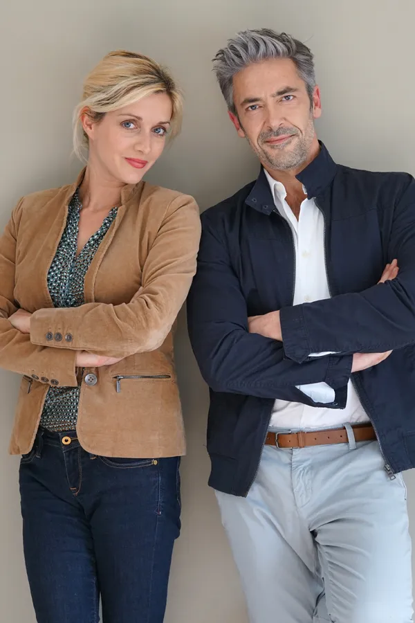 A middle-aged couple stand against a wall smiling with folded arms. Get hyperthyroidism treatment from Vitality Medical in Seattle.