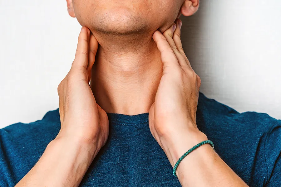 Hypothyroidism-Clinic A man in a dark teal shirt rubs the lymph nodes on his neck. Get hypothyroidism treatment from Vitality Medical in Seattle.