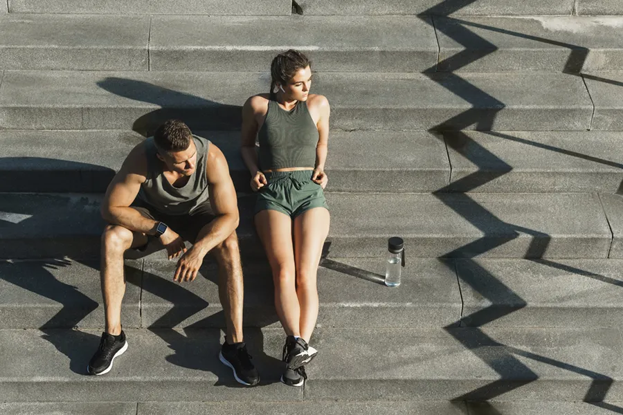 Medical-Weight-Loss-Doctor A couple in gray and green track clothes resting after a workout on stone steps, happy with their weight loss plans from Vitality Medical in Seattle.