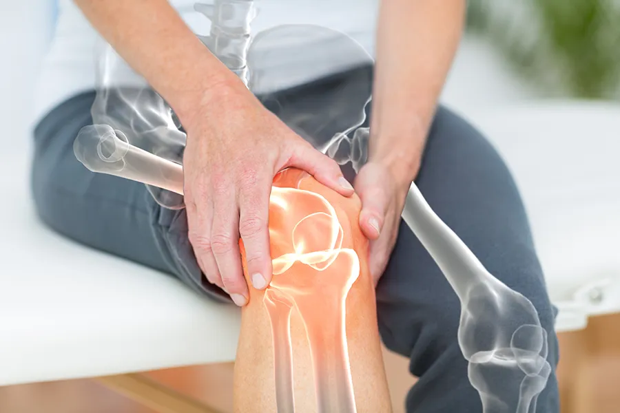 A 3D illustration of the skeleton over the body of a woman who holds her knee in pain, where the area is highlighted. Schedule osteoarthritis treatment from Vitality Medical in Seattle.
