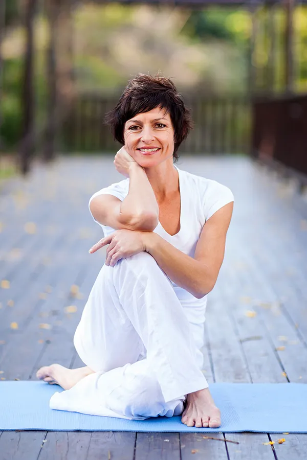 Osteoporosis-Treatment A middle-aged woman happily sits in a yoga pose. Get Osteoporosis treatment from Vitality Medical in Seattle.
