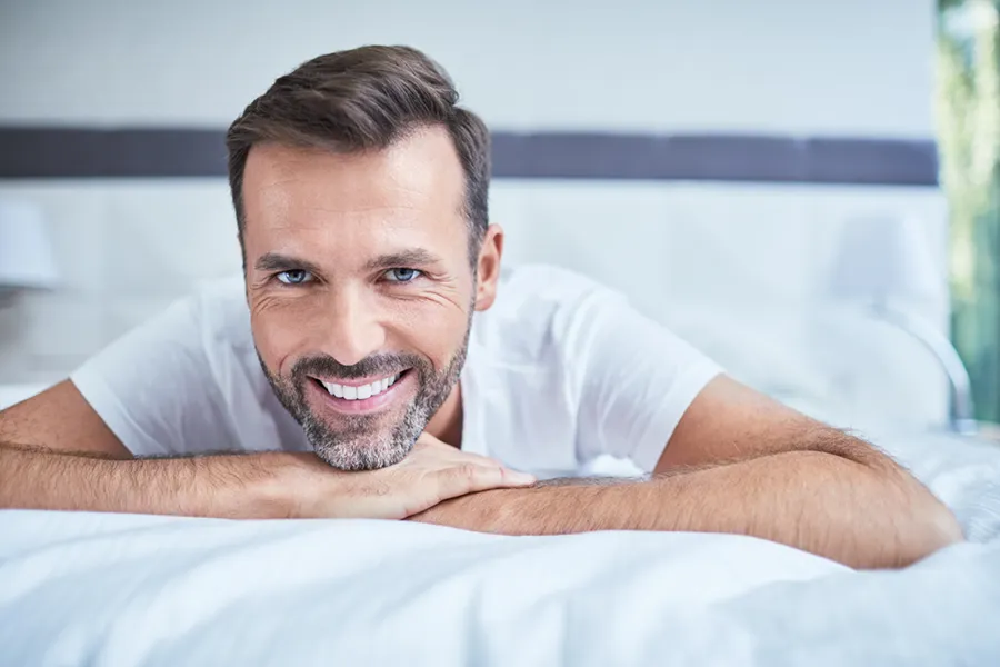 P-Long-Protocol-Clinic A middle-aged man lays on a bed smiling. Schedule the P-Long protocol for ED from Vitality Medical in Seattle.