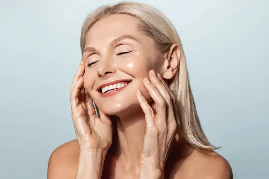 A beautiful mature blonde woman touches her face, happy with her PRP facelift and facial injections from Vitality Medical in Seattle.