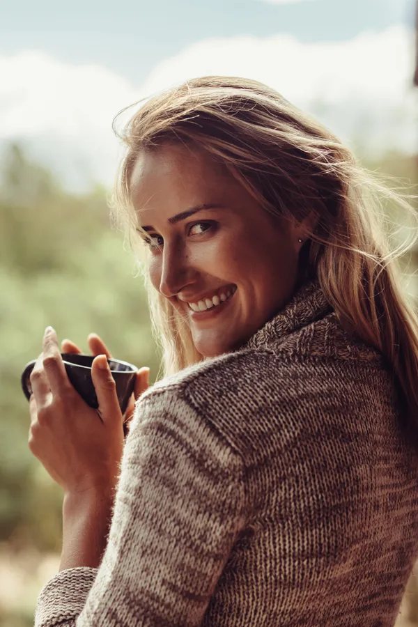 A cozy image of a smiling blonde woman wrapped in a chunky, knit sweater, holding a black coffee mug satisfied with PRP Vaginal Rejuvenation treatment offered by Vitality Medical in Seattle.