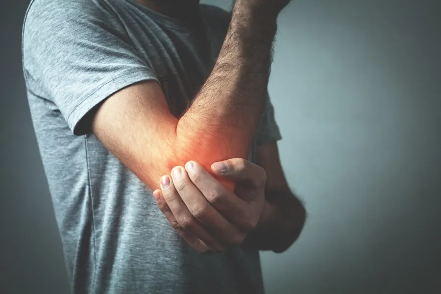 PRP-for-Elbow-Injuries-Doctor A man in a gray t-shirt holds his elbow in pain, considering PRP treatments for elbow pain from Vitality Medical in Seattle.