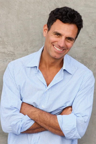 A happy middle-aged man folds his arms and leans against a wall. Get PRP for penis enlargement from Vitality Medical in Seattle.