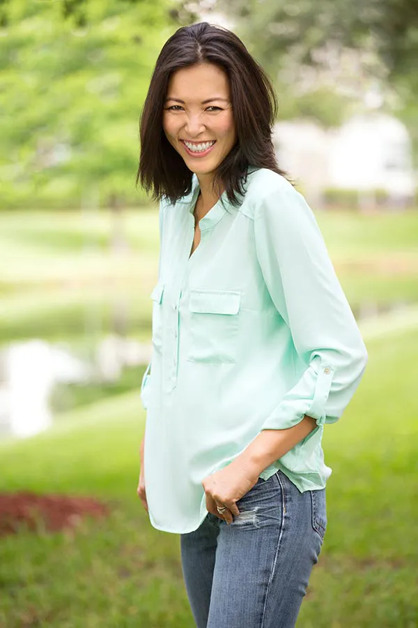 A middle-aged brunette woman in a light green button-up shirt stands outside smiling, happy with her perimenopause treatment from Vitality Medical in Seattle.