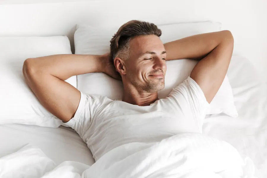 Peyronies-Disease-Clinic A smiling man lays in bed with his hands behind his head. Get treatment for Peyronies Disease from Vitality Medical in Seattle.