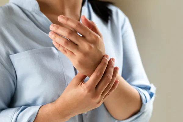 Rheumatoid-Arthritis-Clinic Close up of a woman in a blue blouse rubbing her wrist. Get rheumatoid arthritis treatment from Vitality Medical in Seattle.