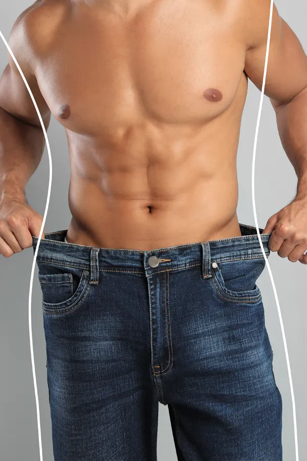 A strong shirtless man in jeans holds the waistlines of his too-big jeans to show the success of semaglutide weight loss from Vitality Medical in Seattle.