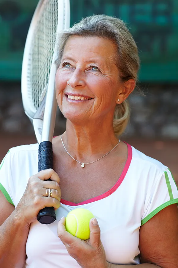 A happy middle-aged woman holds a tennis racquet and ball. Get treatment for tennis elbow from Vitality Medical in Seattle.