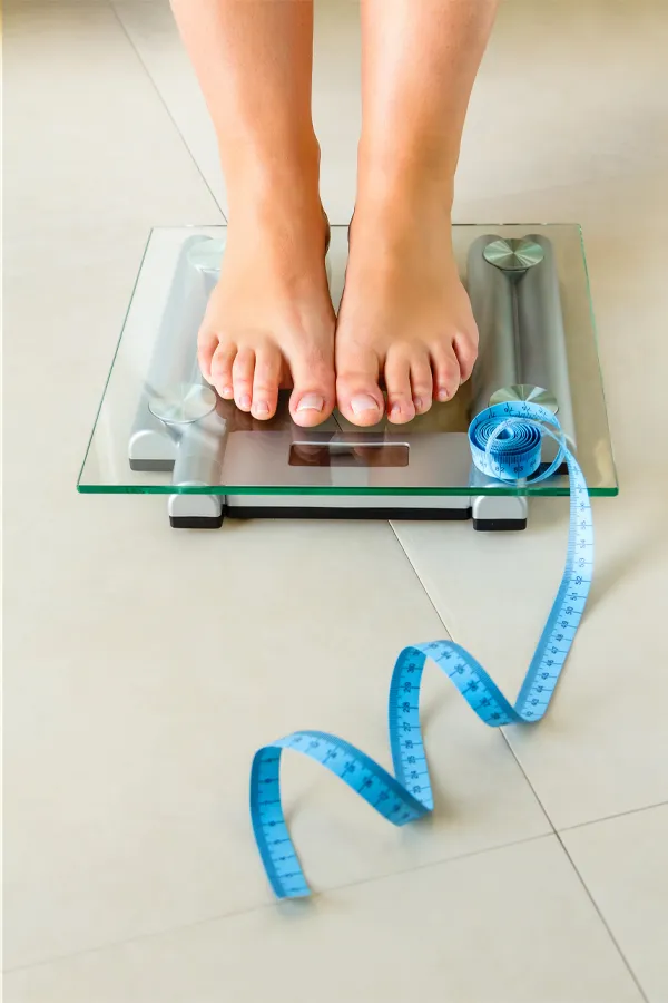 Weight-Loss-Resistance-Treatment Close-up of a woman's feet standing on a scale, with measuring tape by her toes, getting treatment for weight loss resistance from Vitality Medical in Seattle.